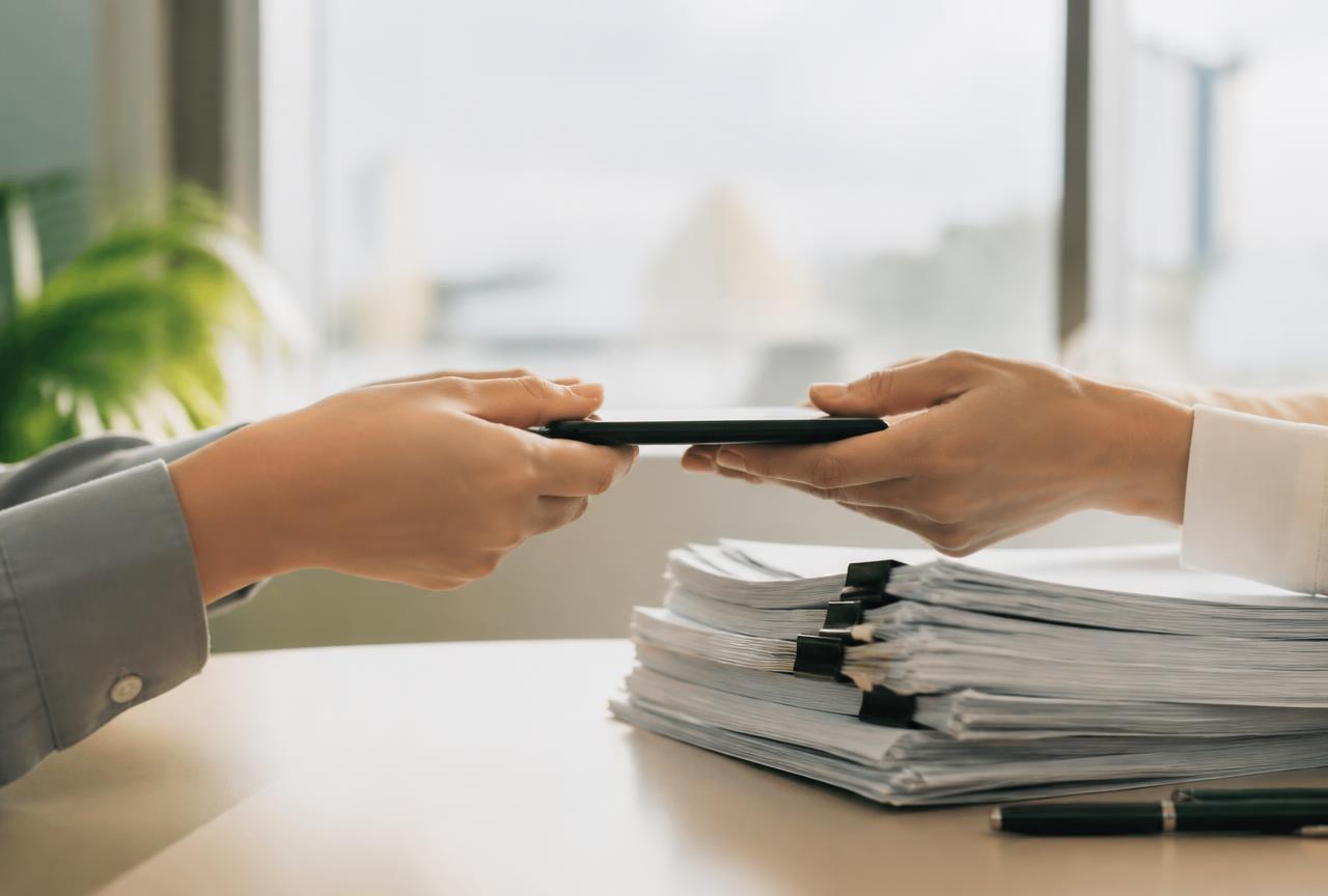 Paperwork and a phone being handed across a bright desk